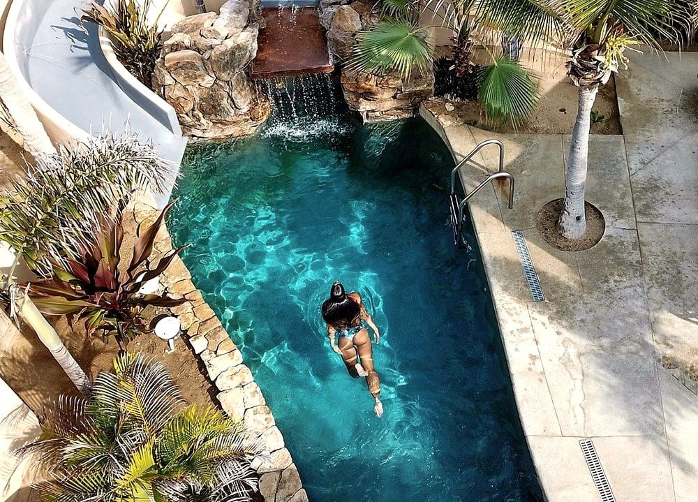 The turquoise pool and waterslide from above, framed by palms and the beach