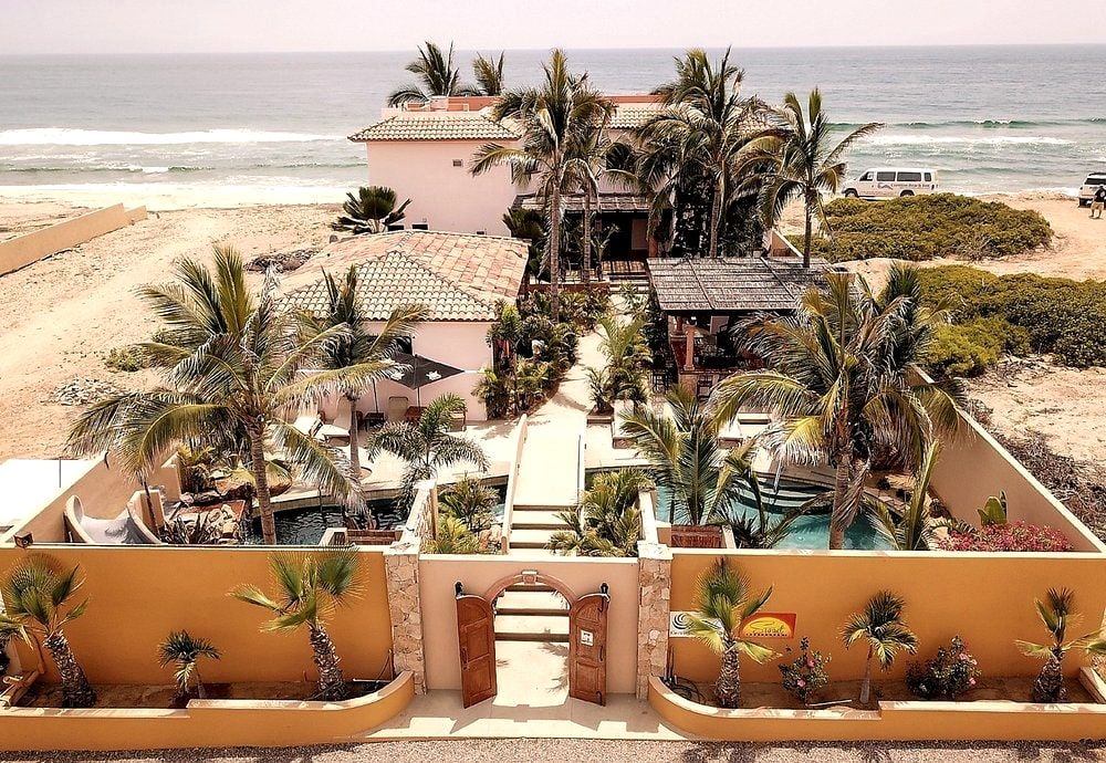 Aerial view of The Cerritos Beach Inn, its palm-shaded courtyard and terracotta roofs set directly on the sand at Playa Los Cerritos