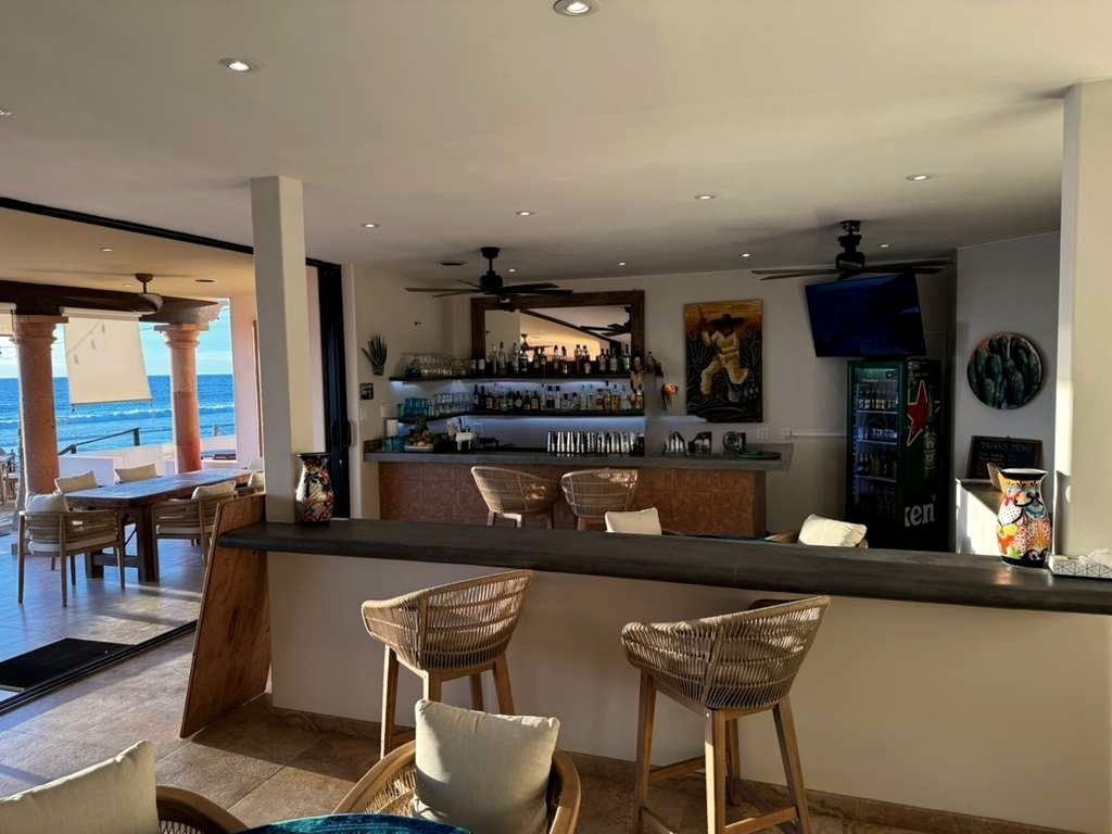 The bar at The Sunset, bottles lined along the back counter and woven stools at the rail