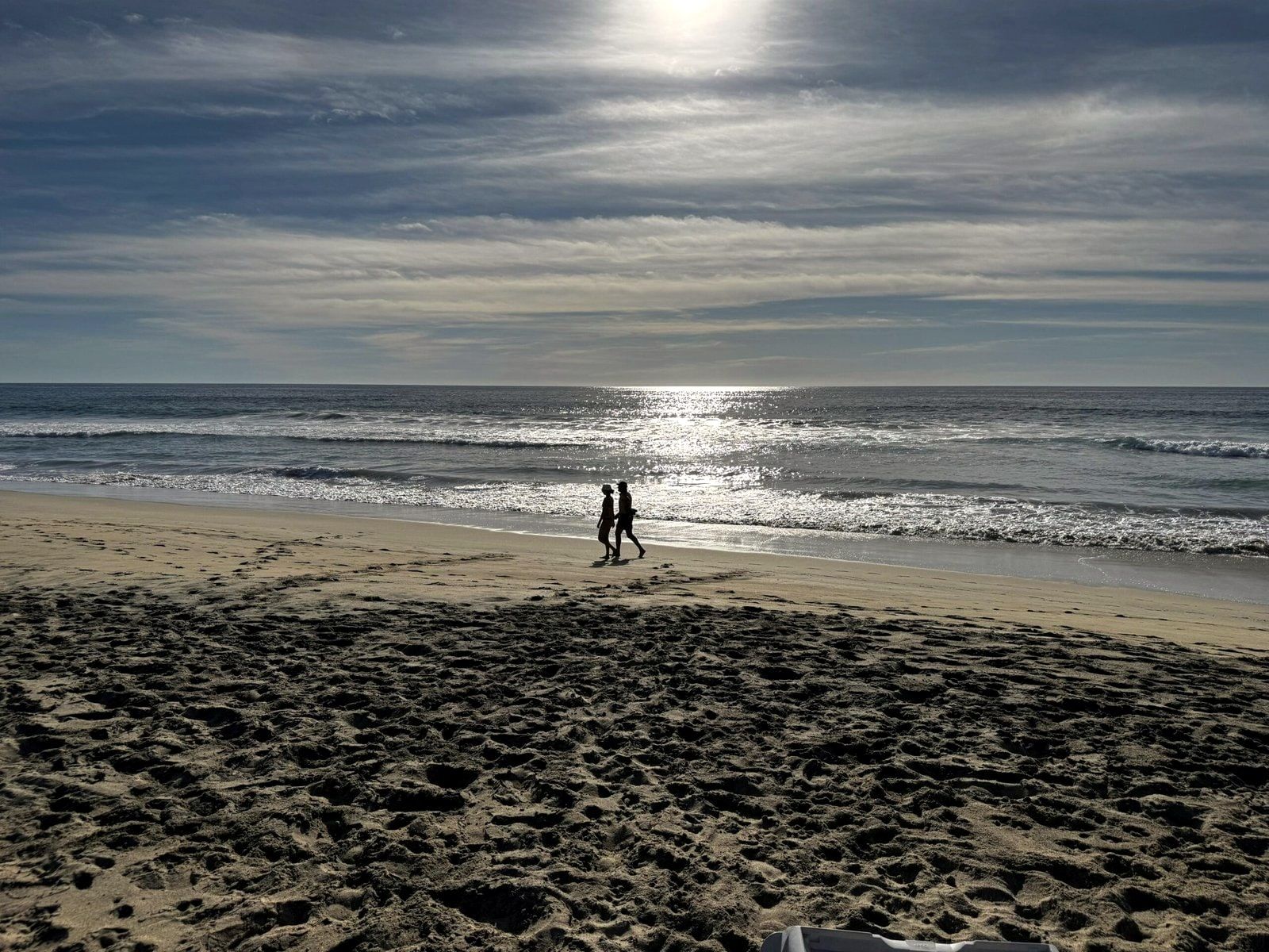 Two people walking the empty shoreline as the sun goes down