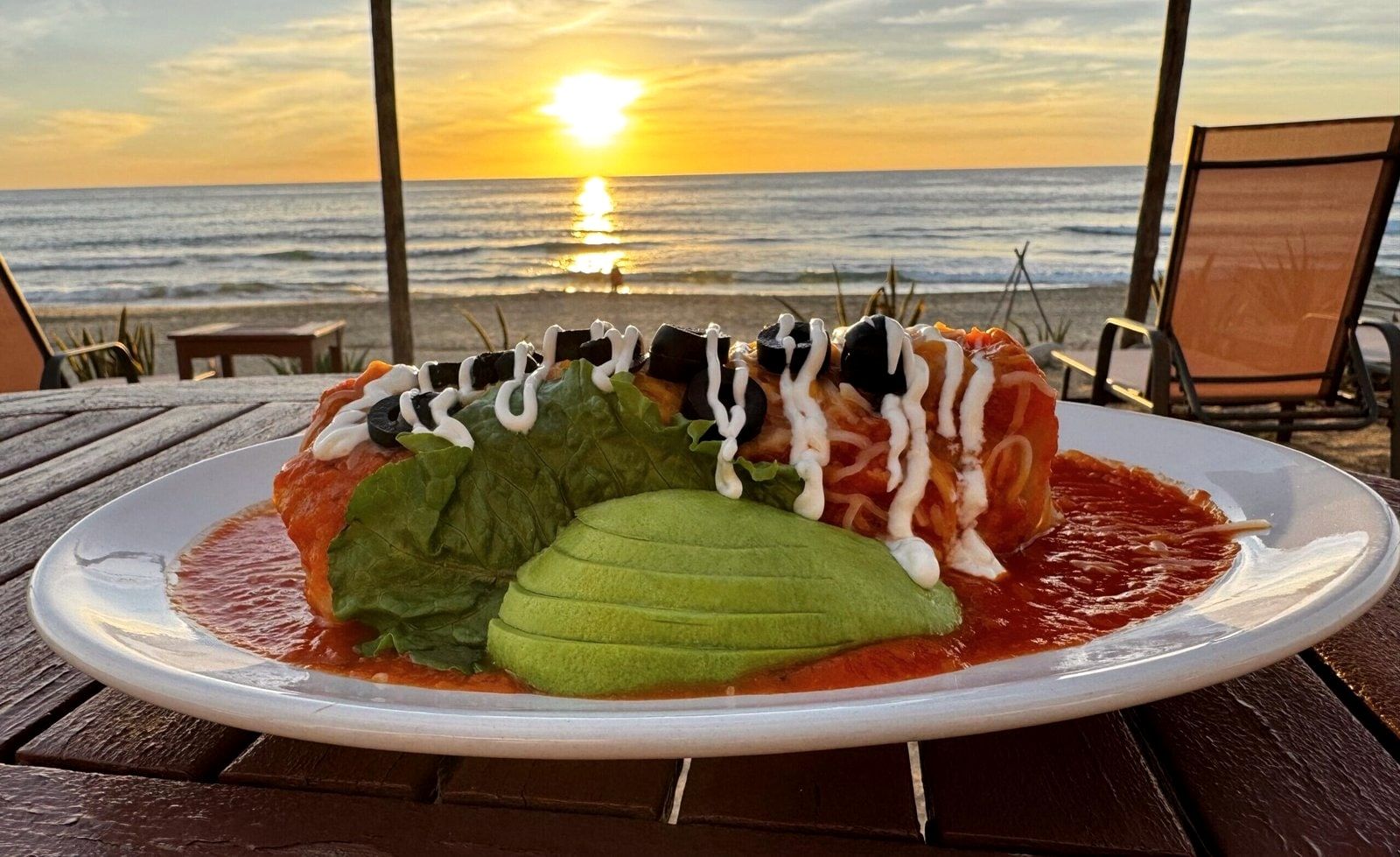 Enchiladas under red sauce with avocado and crema