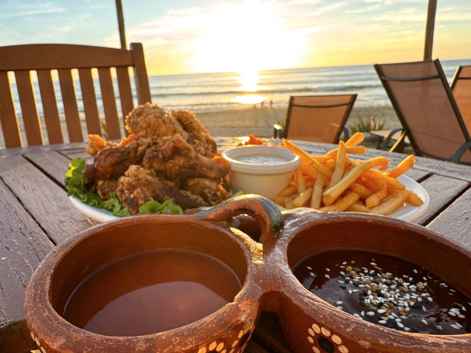 Fried chicken, french fries and clay cups on a table facing the setting sun