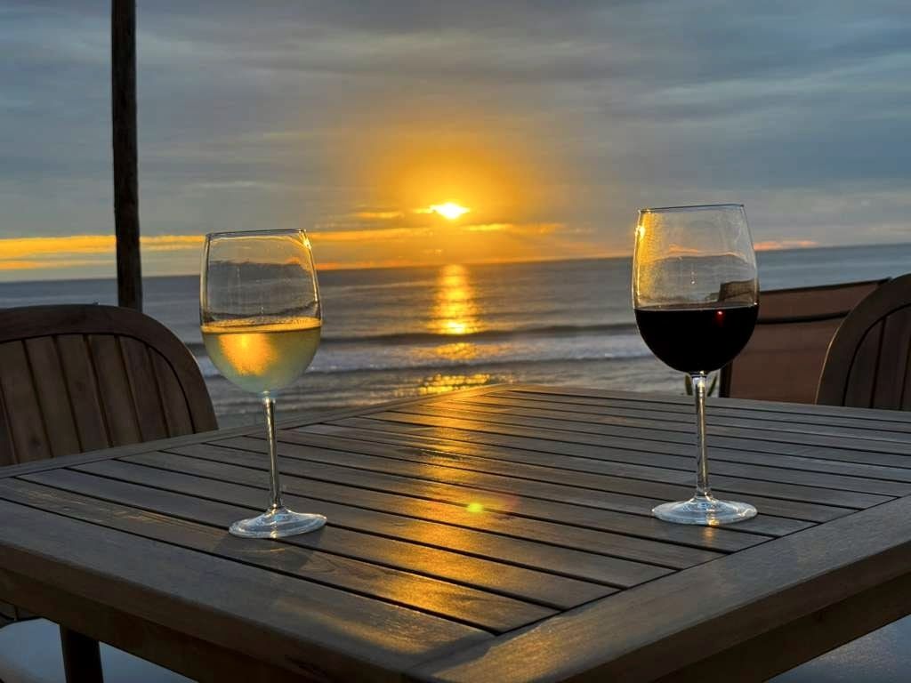 Two glasses of wine on a wooden table, the sun setting on the water behind