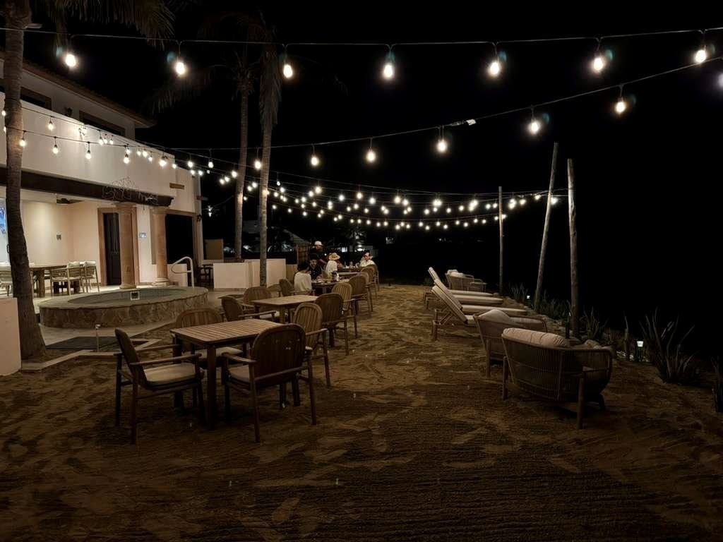 The beachfront patio at night, tables set beneath strings of warm lights