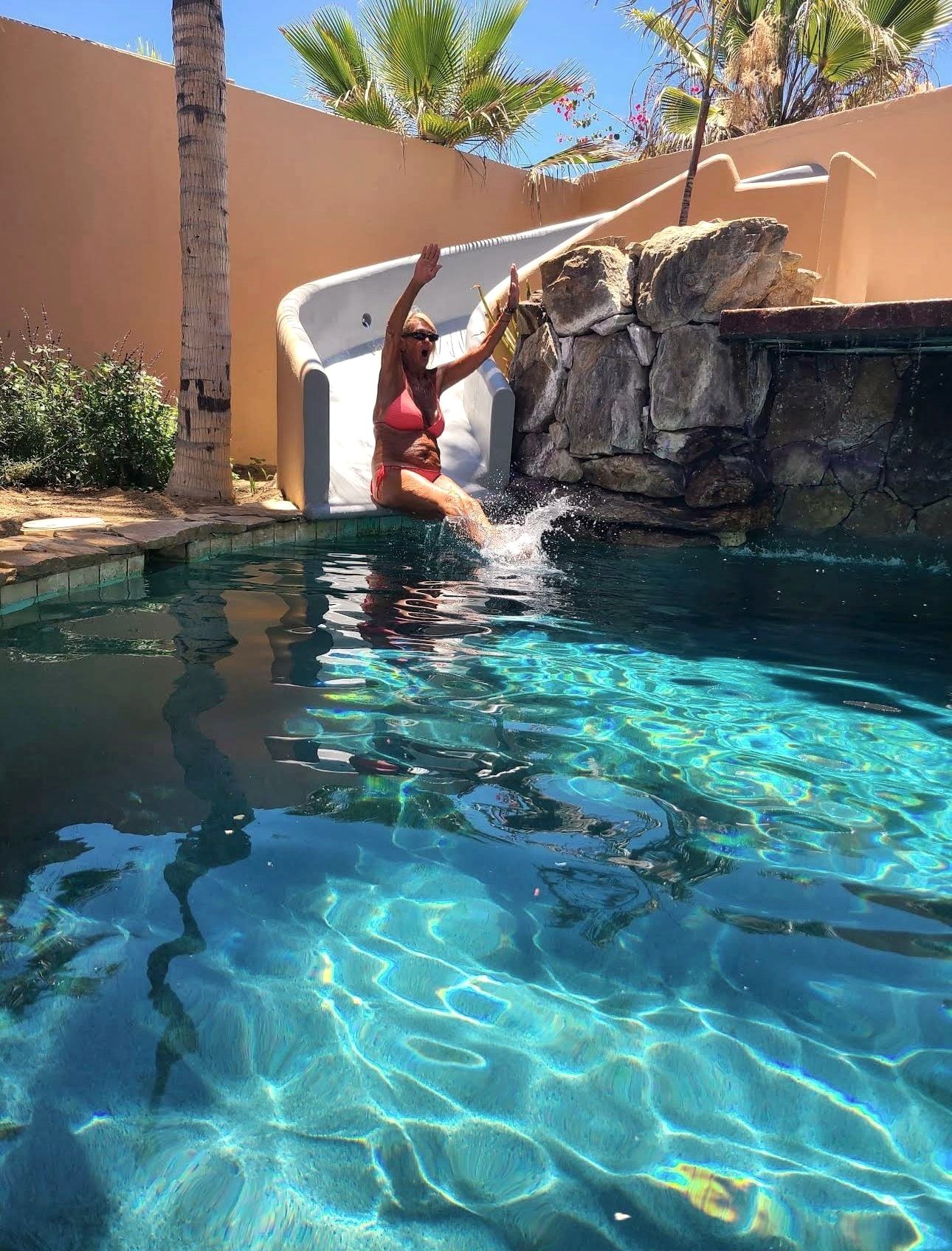A guest coming down the waterslide into the pool on a bright afternoon