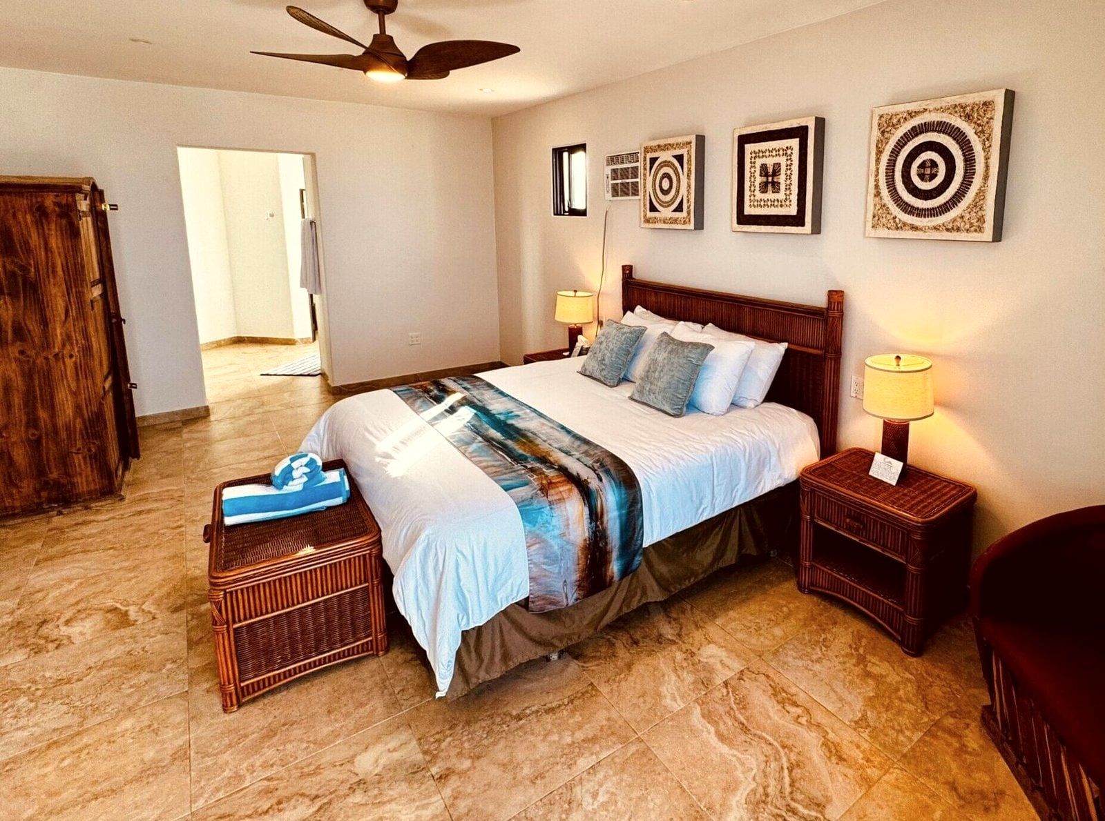 A Deluxe King room facing inland, with hardwood armoire, ceiling fan and framed local artwork